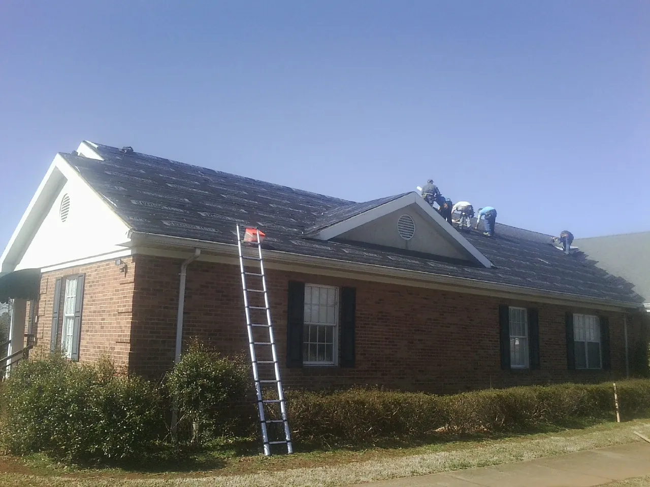 Crew tearing shingles off a brick ranch roof with a ladder set — Emergency Roof Repair work by our crew in Durham