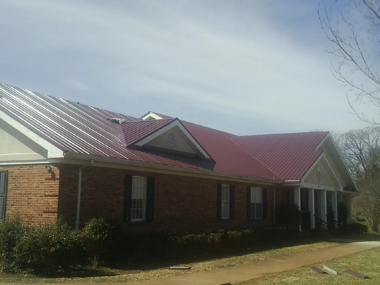 Red metal roof with gabled entries on a long brick building, from a Hail Damage Roof Repair job in Durham